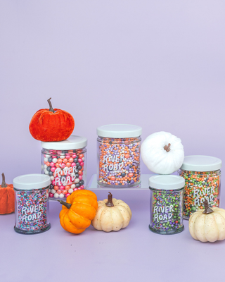 5 sprinkle jars on display along miniature cloth pumpkins.